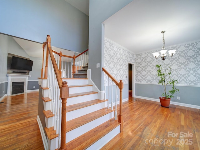 stairway with wood-type flooring, ornamental molding, and a notable chandelier