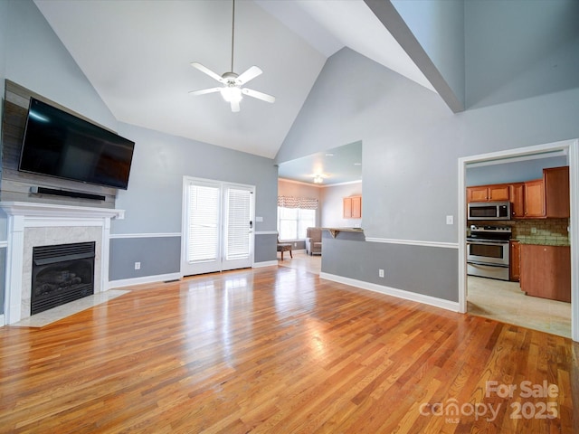 unfurnished living room featuring ceiling fan, a high end fireplace, light hardwood / wood-style floors, and high vaulted ceiling