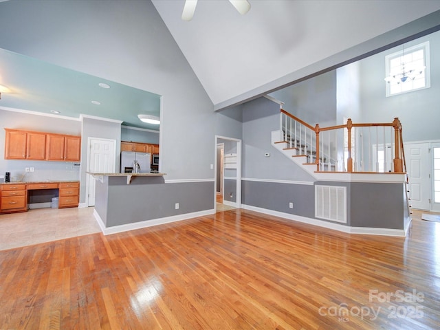 unfurnished living room featuring ceiling fan, light hardwood / wood-style floors, high vaulted ceiling, and built in desk