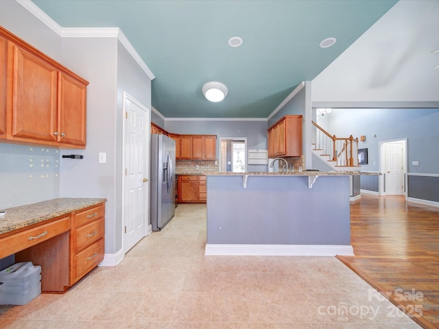 kitchen with stainless steel fridge, a kitchen bar, decorative backsplash, ornamental molding, and light stone countertops