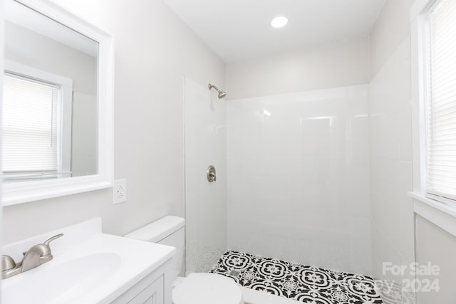 bathroom with toilet, a tile shower, and vanity