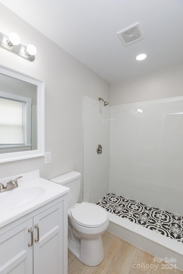 bathroom featuring toilet, a tile shower, hardwood / wood-style flooring, and vanity