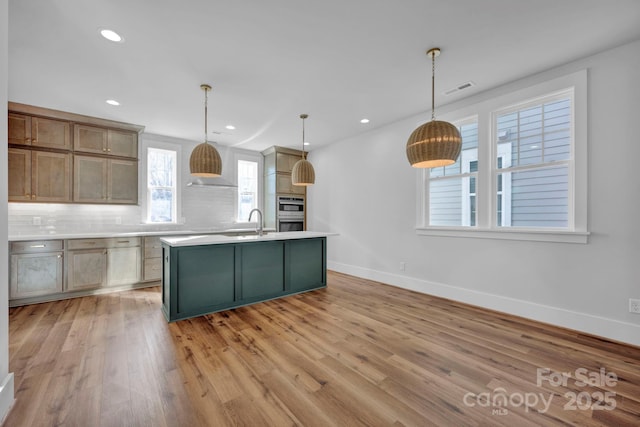 kitchen with decorative light fixtures, backsplash, light hardwood / wood-style flooring, and an island with sink