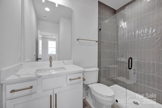 bathroom with toilet, vanity, and a shower with shower door