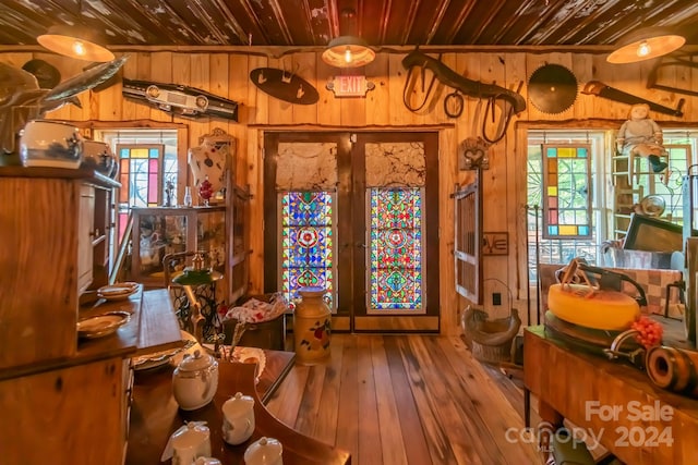 living area featuring a healthy amount of sunlight, wood-type flooring, wooden walls, and french doors