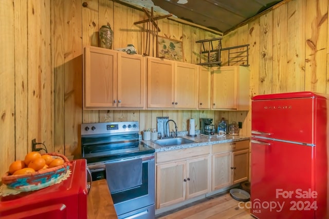 kitchen featuring wooden walls, stainless steel electric range, fridge, sink, and light hardwood / wood-style floors