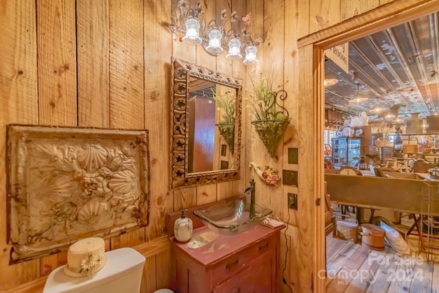 bathroom featuring toilet, hardwood / wood-style flooring, wood walls, and sink