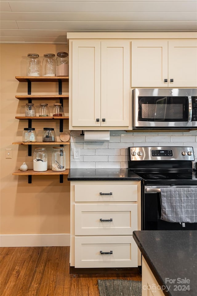 kitchen featuring appliances with stainless steel finishes, dark hardwood / wood-style floors, dark stone counters, and decorative backsplash