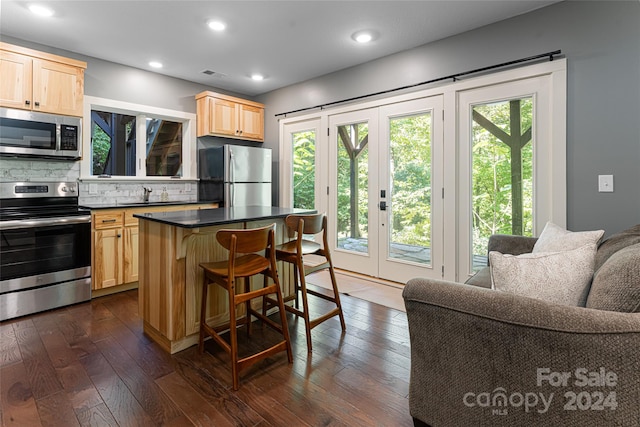 kitchen featuring a center island, stainless steel appliances, dark hardwood / wood-style flooring, a breakfast bar area, and backsplash