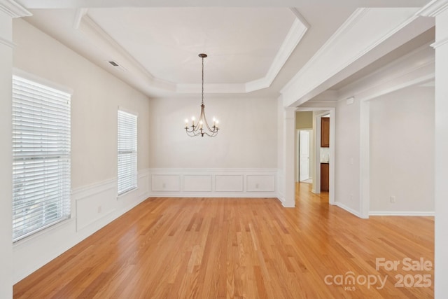 unfurnished dining area with a notable chandelier, a tray ceiling, light hardwood / wood-style floors, and a wealth of natural light