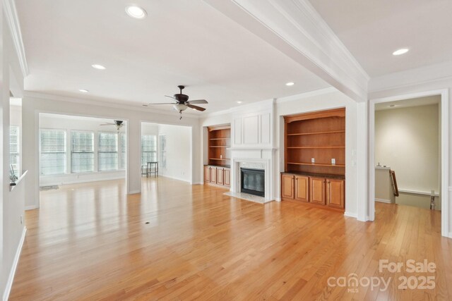 unfurnished living room with ceiling fan, ornamental molding, light hardwood / wood-style flooring, a premium fireplace, and built in shelves