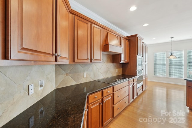 kitchen with pendant lighting, custom range hood, black electric cooktop, dark stone counters, and ornamental molding