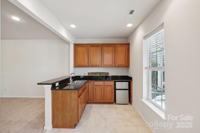 kitchen with kitchen peninsula, a healthy amount of sunlight, dark stone counters, fridge, and sink