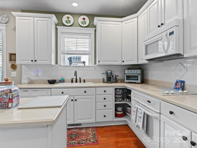 kitchen with hardwood / wood-style flooring, sink, white cabinets, backsplash, and white appliances