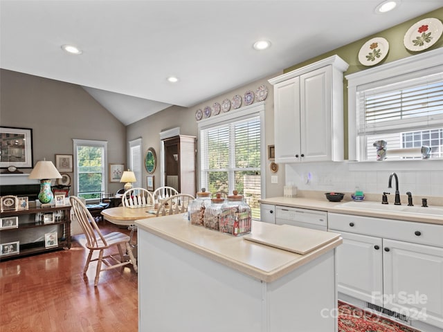 kitchen with white cabinetry, vaulted ceiling, a kitchen island, and sink