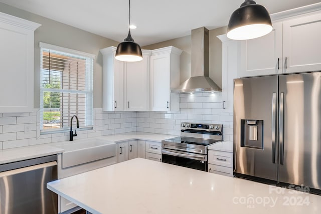 kitchen with white cabinets, decorative light fixtures, appliances with stainless steel finishes, sink, and wall chimney range hood