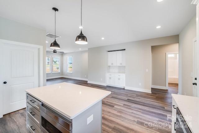 kitchen with hardwood / wood-style floors, a center island, hanging light fixtures, white cabinetry, and stainless steel microwave