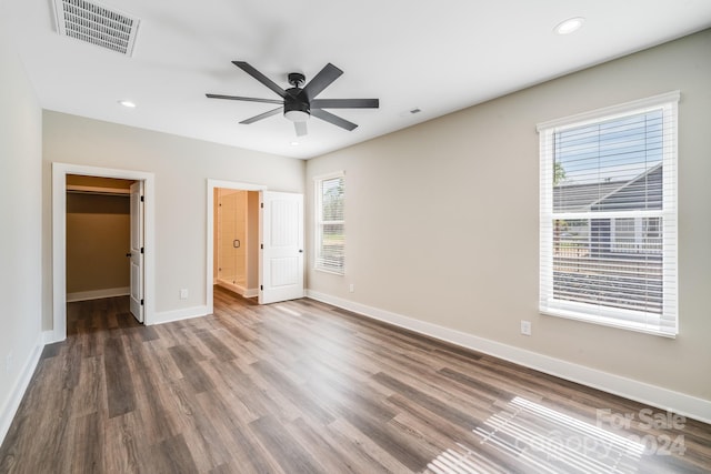 unfurnished bedroom with multiple windows, a walk in closet, ceiling fan, and dark hardwood / wood-style floors