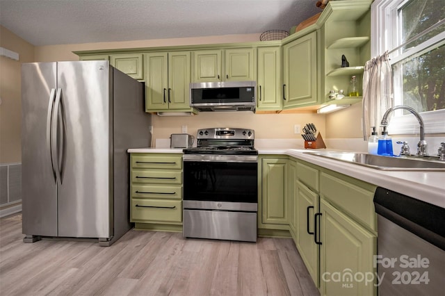 kitchen with appliances with stainless steel finishes, a textured ceiling, light hardwood / wood-style flooring, and sink