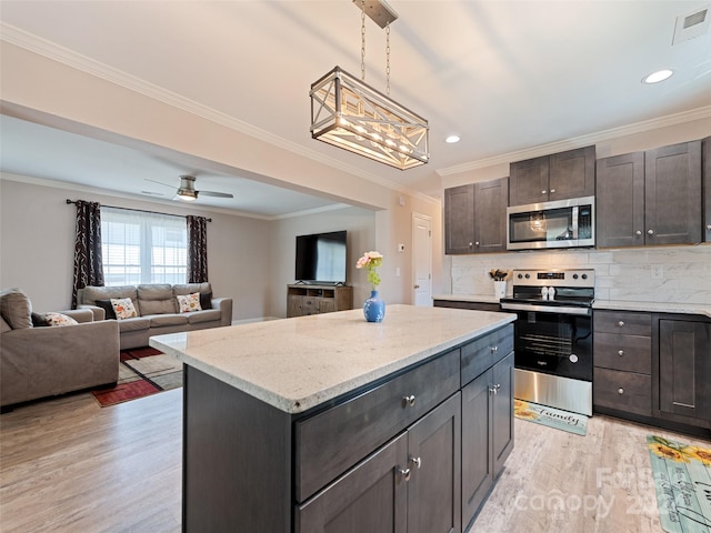 kitchen with ceiling fan with notable chandelier, appliances with stainless steel finishes, a kitchen island, and light hardwood / wood-style floors