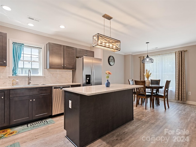 kitchen with pendant lighting, appliances with stainless steel finishes, a center island, sink, and light wood-type flooring