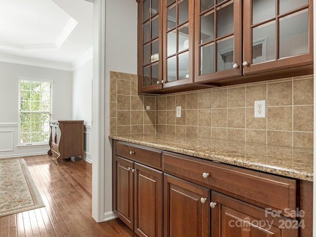 kitchen featuring ornamental molding, backsplash, light stone countertops, dark hardwood / wood-style floors, and a raised ceiling