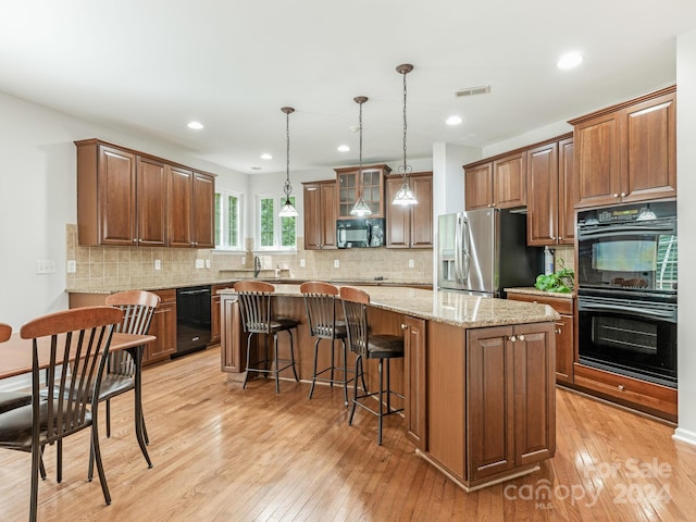 kitchen with black appliances, pendant lighting, a center island, and light hardwood / wood-style flooring