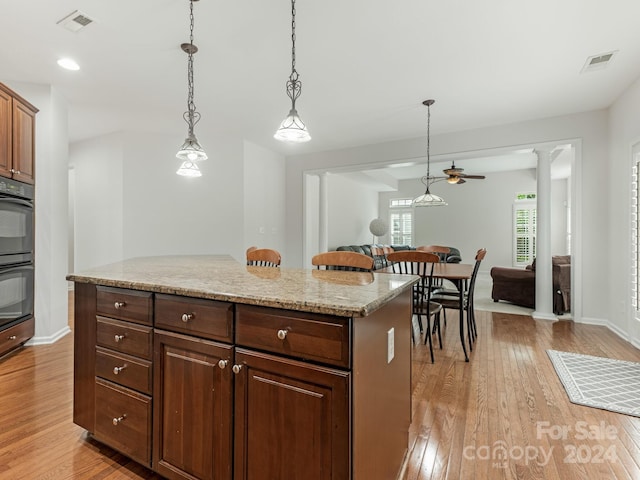 kitchen featuring hanging light fixtures, a center island, light hardwood / wood-style floors, decorative columns, and double oven