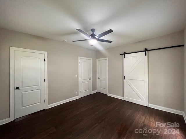 unfurnished bedroom featuring a barn door, ceiling fan, and dark hardwood / wood-style floors