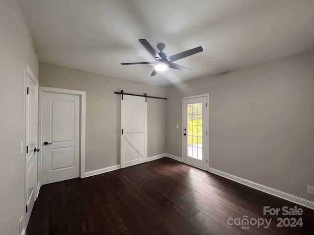 unfurnished bedroom featuring access to exterior, ceiling fan, a barn door, and dark hardwood / wood-style floors