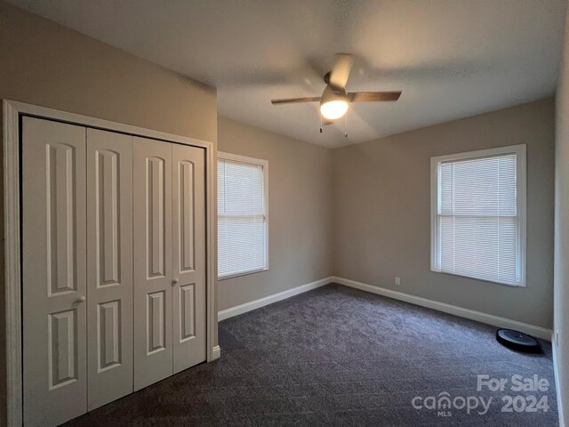 unfurnished bedroom with dark colored carpet, ceiling fan, and a closet