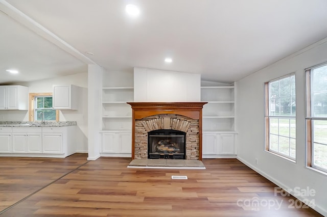 unfurnished living room featuring light wood-type flooring, lofted ceiling, sink, and built in shelves