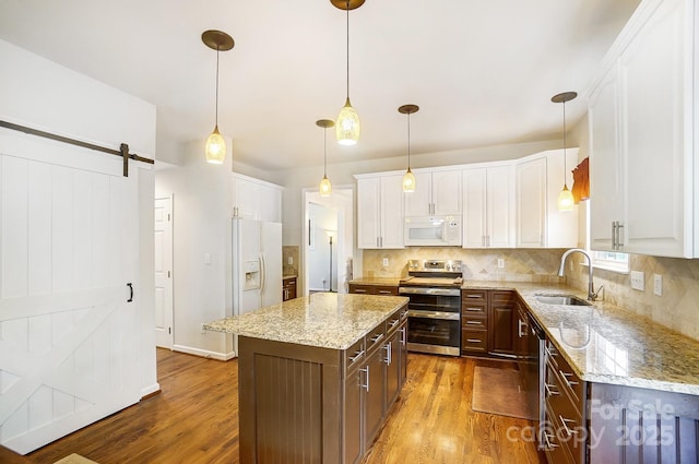 kitchen featuring white cabinetry, a barn door, a kitchen island, sink, and white appliances