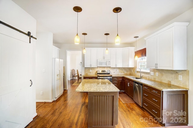 kitchen with appliances with stainless steel finishes, a center island, pendant lighting, and a barn door