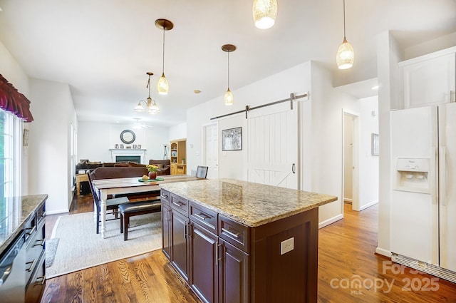 kitchen featuring white fridge with ice dispenser, hardwood / wood-style flooring, decorative light fixtures, a barn door, and dark brown cabinets