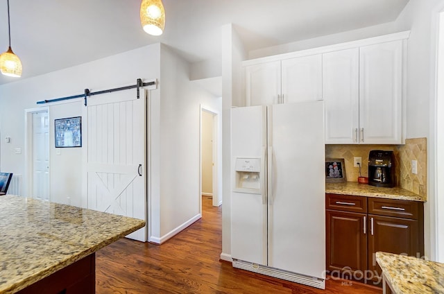 kitchen featuring light stone counters, white fridge with ice dispenser, pendant lighting, a barn door, and white cabinets