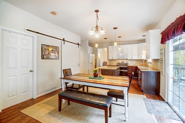 dining room with sink, dark wood-type flooring, an inviting chandelier, and a barn door