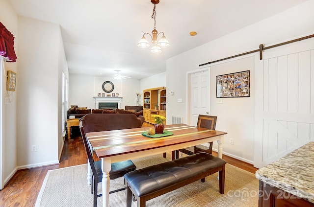 dining room featuring ceiling fan with notable chandelier, dark hardwood / wood-style floors, and a barn door