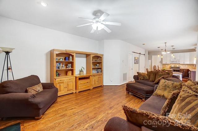 living room featuring ceiling fan, a barn door, and light hardwood / wood-style floors