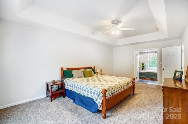 carpeted bedroom with a raised ceiling, ensuite bathroom, and ceiling fan