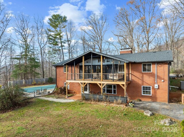 rear view of property featuring a lawn, a covered pool, cooling unit, and a sunroom