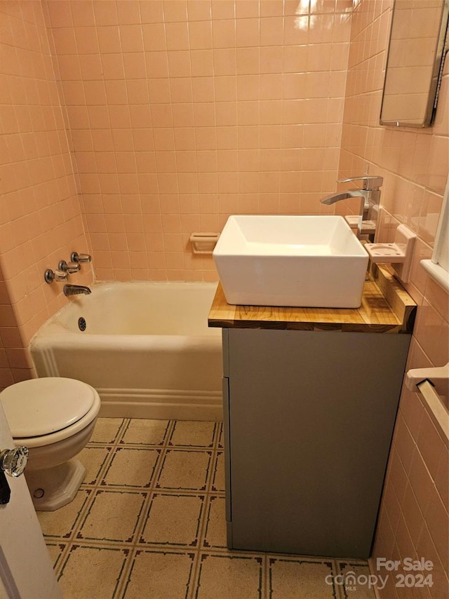 full bathroom featuring tile walls, tiled shower / bath, toilet, and vanity