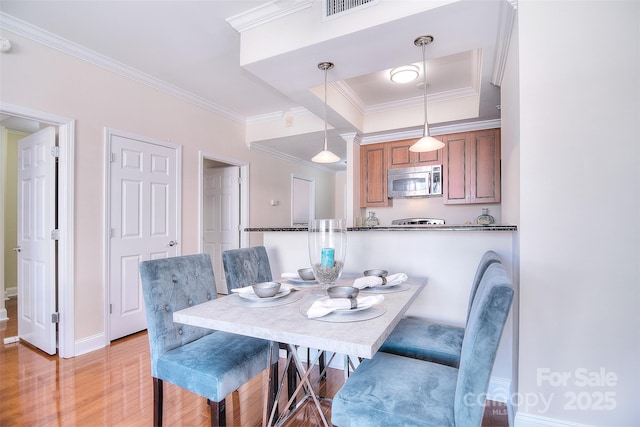 dining room with ornamental molding, light wood-type flooring, visible vents, and baseboards