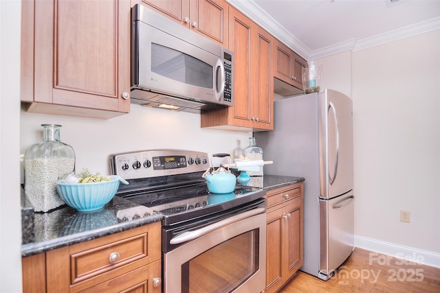 kitchen with light wood finished floors, appliances with stainless steel finishes, brown cabinetry, ornamental molding, and dark stone countertops