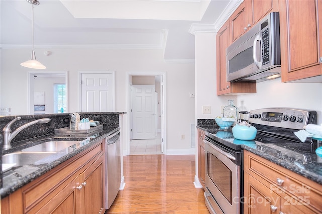 kitchen featuring a sink, hanging light fixtures, appliances with stainless steel finishes, dark stone counters, and brown cabinetry