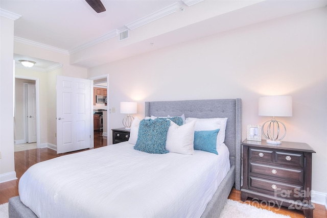 bedroom with crown molding, visible vents, a ceiling fan, wood finished floors, and baseboards