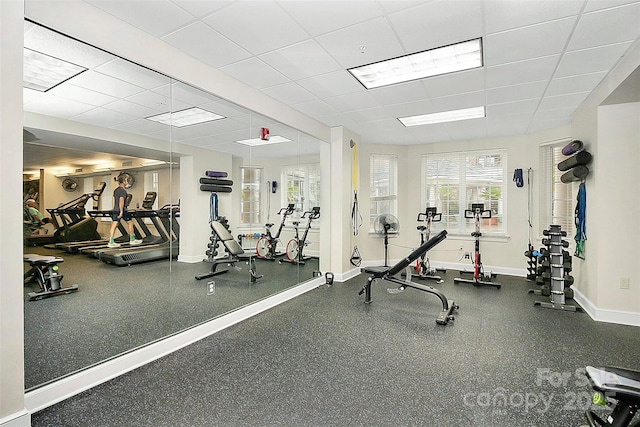 gym with a paneled ceiling and baseboards