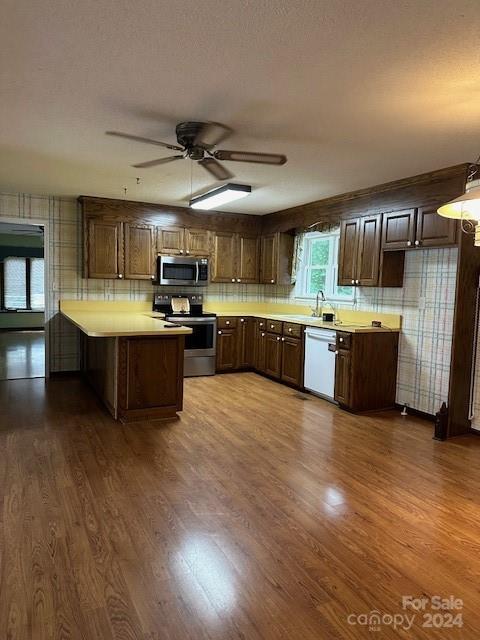 kitchen with stainless steel appliances, hardwood / wood-style floors, kitchen peninsula, and ceiling fan