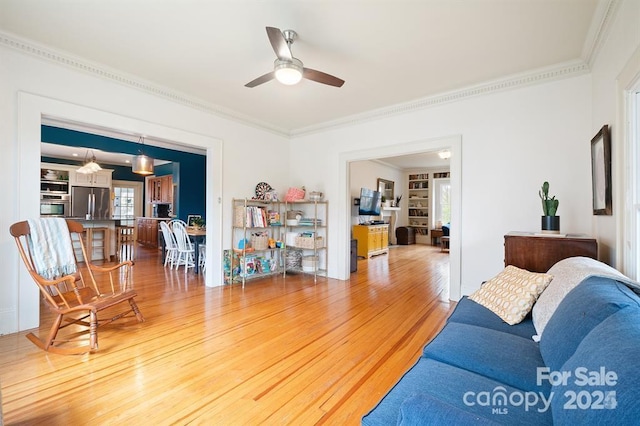 living room with built in shelves, ceiling fan, wood-type flooring, and ornamental molding