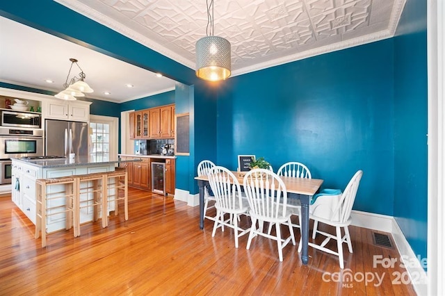 dining space featuring beverage cooler, ornamental molding, and light hardwood / wood-style flooring